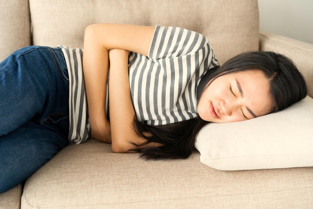 Woman on a sofa holding her stomach due to stomach pain and nausea