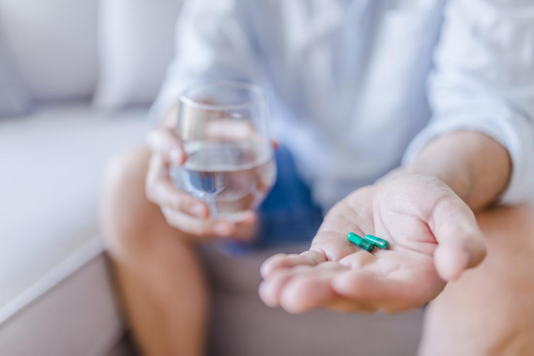 A person holding capsule pills and glass of water